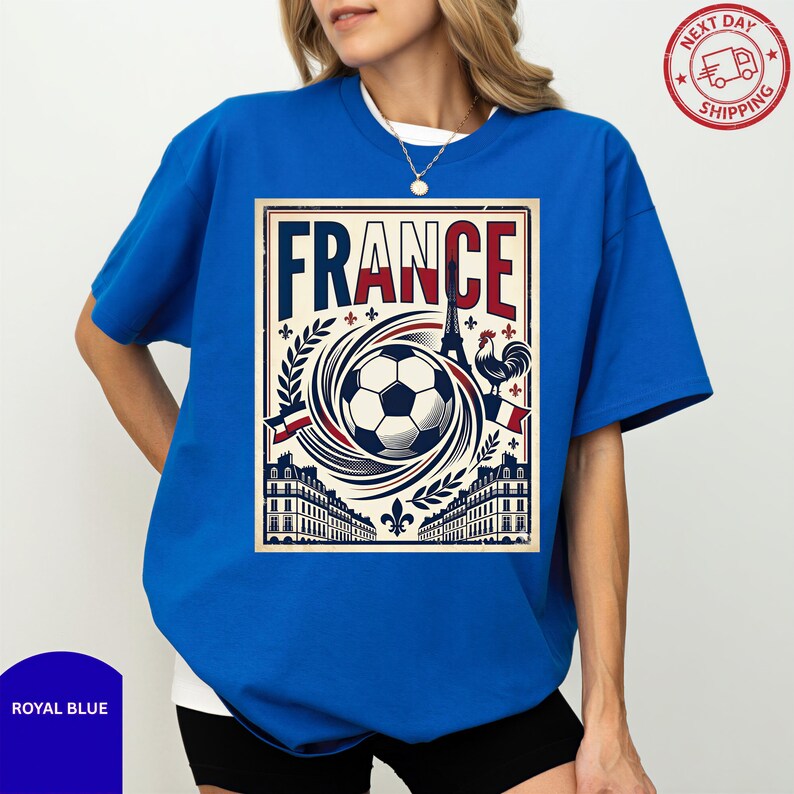 A woman wearing a blue t-shirt with a graphic design featuring a soccer ball, buildings, and a rooster, along with the word "FRANCE" prominently displayed.