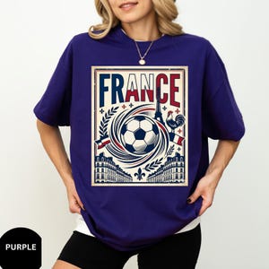 A woman wearing a purple t-shirt with a graphic design featuring a soccer ball, a rooster, and buildings, along with the word "FRANCE" prominently displayed.