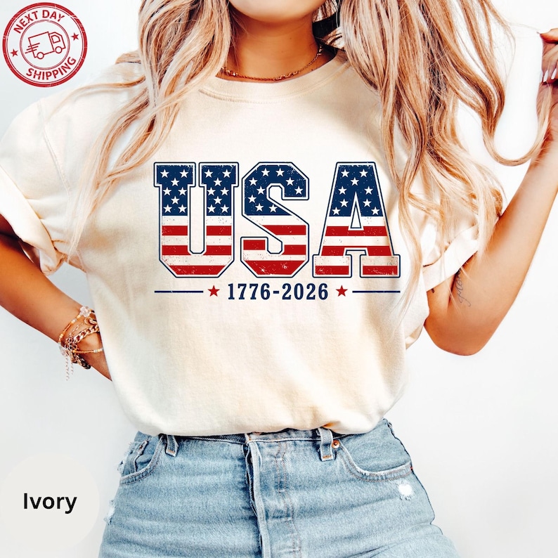 A woman wearing a white t-shirt with the text "USA" printed on it, along with the years 1776-2026.