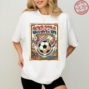 A woman wearing a white t-shirt with a graphic design featuring a soccer ball, flags, and text related to Croatia.