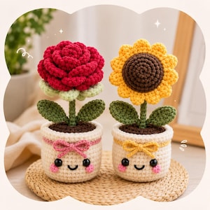 Puede incluir: Dos macetas de flores de ganchillo, una con una rosa roja y otra con un girasol amarillo. Las macetas son de color crema con caras sonrientes, lazos rosas y amarillos y hojas verdes. Las flores están sobre una estera tejida.