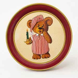 May include: A round metal tray with a deep red rim and a gold-toned edge. The center features a cream-colored background with a small dot pattern, depicting a brown teddy bear wearing a red and white striped nightcap and matching nightshirt.