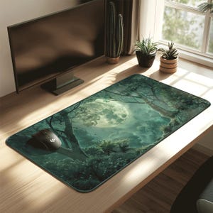 Puede incluir: Una alfombrilla de ratón rectangular con una escena de bosque nocturno y una gran luna brillante. El diseño incorpora árboles, follaje y una paleta de colores oscuros. Un ratón de ordenador negro descansa sobre la alfombrilla, que está sobre un escritorio de madera.