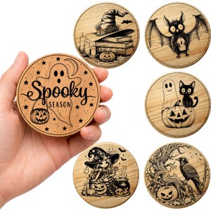 Peut inclure: Ensemble de dessous de verre en bois d'Halloween avec des motifs gravés. L'un des dessous de verre représente un fantôme avec le texte "Spooky Season" et une citrouille. D'autres représentent un chapeau de sorcière, une chauve-souris, un fantôme avec un chat, une sorcière et un corbeau.