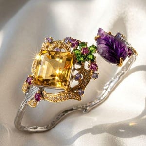 May include: A silver bracelet featuring a large, square, yellow gemstone and a carved purple leaf. The bracelet is decorated with smaller purple, green, and yellow gemstones, set in a gold filigree design.