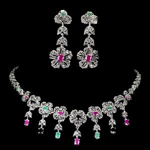 Puede incluir: Un conjunto de joyería compuesto por un collar y un par de pendientes colgantes. Las piezas presentan metal plateado con detalles de marcasita, motivos florales y piedras preciosas ovaladas de color rosa y verde engastadas.