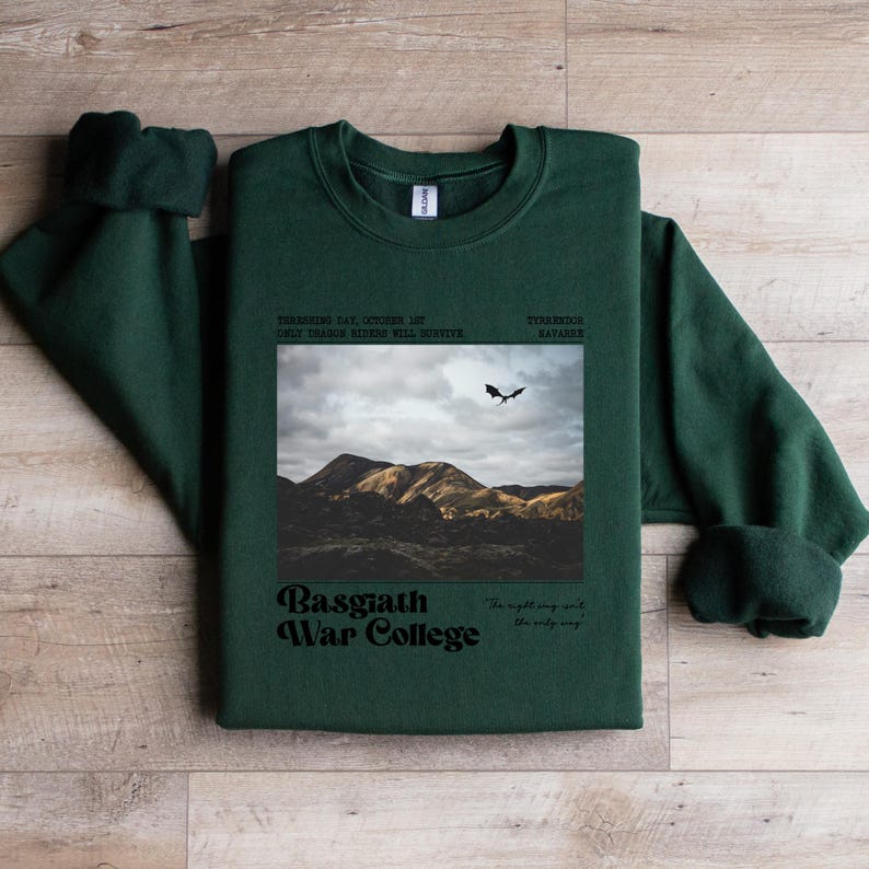 May include: Dark green sweatshirt with a graphic featuring a mountain landscape, a flying dragon, and the text "Basgiath War College." Additional text includes "Only Dragon Riders Will Survive" and "The night sing with the only way."