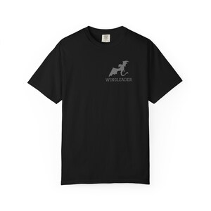 May include: A black short-sleeve t-shirt featuring a grey graphic on the left chest. The graphic depicts a silhouette of a dragon in flight positioned above the text WINGLEADER in a bold, sans-serif font. The shirt has a crew neckline.