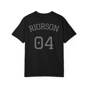 May include: A black short-sleeved t-shirt featuring the name RIORSON in a grey arched font above the number 04 in a large grey block-style font. The design is centered on the back of the shirt, displaying a clean, athletic-inspired aesthetic.