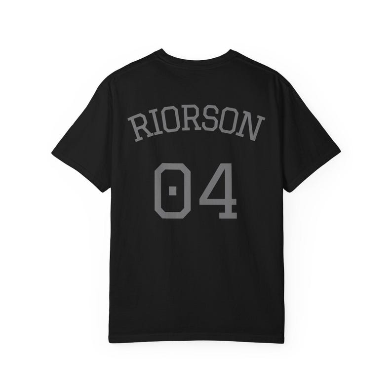 May include: A black short-sleeved t-shirt featuring the name RIORSON in a grey arched font above the number 04 in a large grey block-style font. The design is centered on the back of the shirt, displaying a clean, athletic-inspired aesthetic.