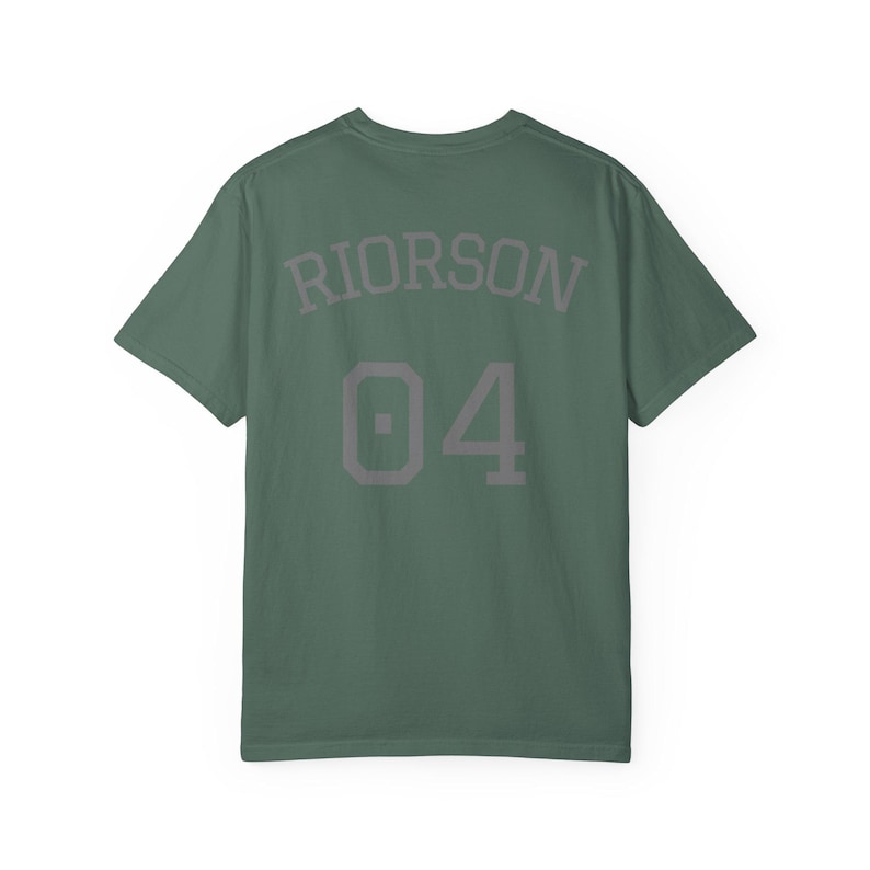 May include: A sage green short-sleeve t-shirt featuring the text RIORSON arched above the number 04 in a dark grey block font. The garment has a crew neckline and a standard fit, displaying a clean design on the back of the shirt.