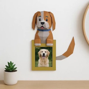 May include: A brown and white paper dog decoration with a blue collar, above a yellow framed photo of a golden retriever. The dog has a tail extending to the right. A small succulent plant in a white pot sits on a wooden surface.