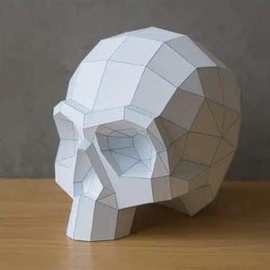 Può includere: Un teschio di carta bianco geometrico con contorni neri. Il teschio è costruito da più forme piatte, triangolari e quadrilatere, creando un aspetto sfaccettato. Il teschio è posizionato su una superficie di legno, con uno sfondo grigio neutro.