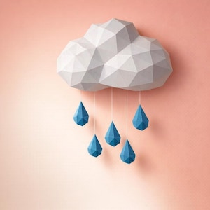 Puede incluir: Una nube de papel geométrica con seis gotas de lluvia azules en forma de lágrima colgando debajo. La nube es blanca y gris, y el fondo es de color rosa claro. Un artículo decorativo.