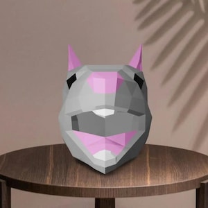 May include: A geometric, low-poly style sculpture of a rabbit's head. The sculpture is primarily gray with pink accents on the ears and mouth. It sits on a small, round wooden table with a neutral background.