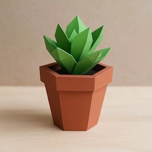 Peut inclure: Une plante succulente en papier dans un pot hexagonal marron. La succulente a plusieurs feuilles vertes pointues. Le pot est de couleur marron chaud et repose sur une surface claire. Le design général est géométrique et moderne.