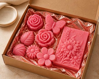 May include: A cardboard gift box lined with metallic pink paper containing several pink wax or soap shapes. The set includes two roses, a butterfly, two leaves, two small flowers, and one large rectangular bar embossed with a detailed floral design.