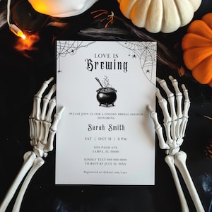 May include: A white rectangular bridal shower invitation with black text reading Love is Brewing, featuring a central illustration of a cauldron, spider web corner accents, and event details for Sarah Smith on October 31 at 6 PM in Tampa, FL.