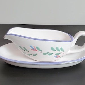 May include: White ceramic gravy boat and saucer set. The gravy boat has a handle and a spout, with a pale blue rim. The set is decorated with green and pink floral designs. The saucer has a matching pale blue rim.