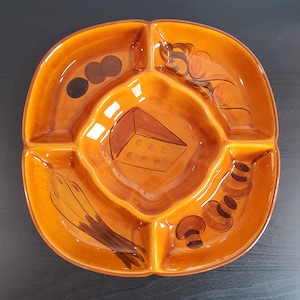 May include: A square, divided serving dish with a glossy, orange-brown glaze. The dish features four sections, each decorated with painted food illustrations, including cheese, mushrooms, and olives. The dish is designed for serving appetizers or snacks.