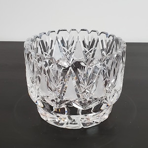 May include: A clear, cut-crystal bowl with a detailed geometric pattern. The bowl has a wide, rounded shape with a scalloped rim. The intricate design features repeating shapes and lines, creating a sparkling effect. The bowl is likely used for decorative purposes.