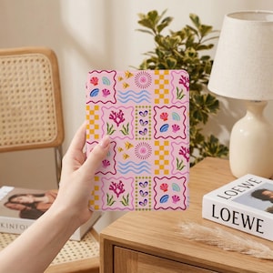 May include: A pink patterned notebook featuring a colorful ocean-themed design. The design includes coral, fish, seashells, and wavy lines. The notebook is held in a person's hand.