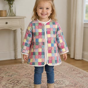 May include: A long-sleeved quilted jacket featuring a colorful patchwork pattern of squares in shades of pink, blue, yellow, and green. The jacket has a round neckline, white trim along the edges, and a front opening. It is worn with blue denim jeans.