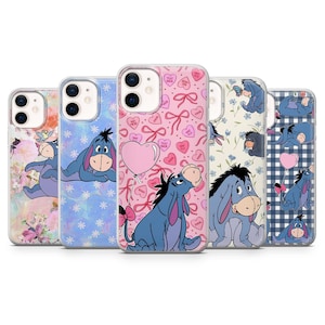 May include: Five phone cases displaying Eeyore from Winnie the Pooh. The cases feature diverse designs, such as floral, heart, and bow patterns, with Eeyore in different poses. The cases are in a variety of colours, including pink, blue, and white.