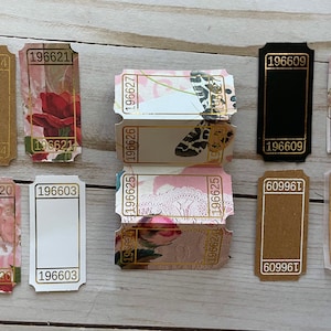 May include: A collection of ten vintage ticket-style paper tags with gold trim and various designs. The tags feature floral patterns, butterflies, and text including the numbers 196620, 196603, 196625, 196626, 196627, 196609, 196642, 60996T, and 196620.