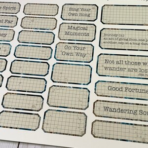 May include: A set of 14 rectangular stickers with a grid pattern and blue trim. The stickers feature inspirational quotes and phrases, including "Free Spirit", "Travel Far", "Journey", "Magic", "Wander", "Sing Your Own Song", "Magical Moments", "Go Your Own Way", "Not all those who wander are lost...", "Good Fortune", and "Wandering Soul".