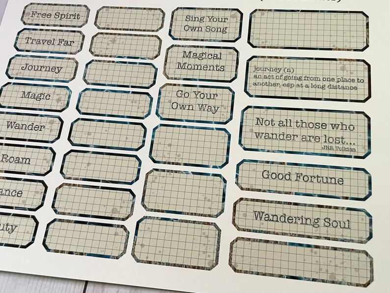 May include: A set of 14 rectangular stickers with a grid pattern and blue trim. The stickers feature inspirational quotes and phrases, including "Free Spirit", "Travel Far", "Journey", "Magic", "Wander", "Sing Your Own Song", "Magical Moments", "Go Your Own Way", "Not all those who wander are lost...", "Good Fortune", and "Wandering Soul".