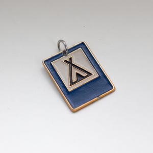 May include: A rectangular pendant with a blue border and a silver centre. The centre features a black and gold symbol resembling a teepee. The pendant has a gold trim and a silver loop for attachment.