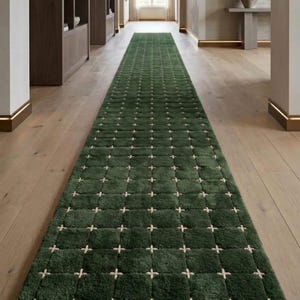 May include: A long, rectangular green rug with a grid pattern of white cross-stitch designs. The rug is made of a plush material and is placed in a hallway with wooden flooring. The rug's dimensions are approximately 10 feet long.