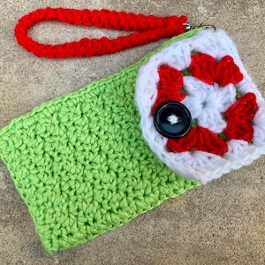 May include: A handmade crochet wallet with a Granny Square design. The wallet features a bright green base, a white and red Granny Square flap, a black button closure, and a red wrist strap.