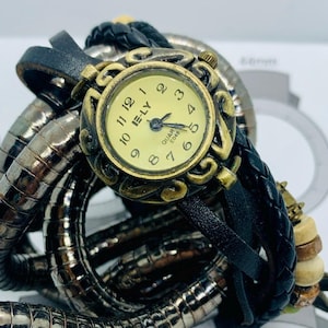 May include: A vintage-style watch with a round, gold-toned face and black leather straps. The watch face displays the text "IE-LY QUAR E048". The watch is surrounded by a silver-toned, coiled metal band and wooden beads.