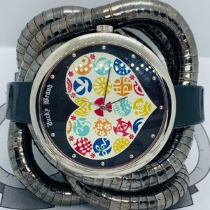 Peut inclure: Une montre Lucky Brand avec un boîtier argenté et un cadran noir orné d'un motif en forme de cœur rempli de motifs floraux colorés. La montre a un bracelet vert foncé et un bracelet enroulé argenté.
