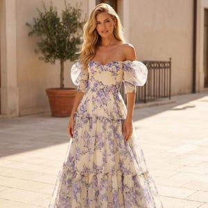 May include: A cream-coloured, off-the-shoulder floral dress with a sweetheart neckline and puff sleeves. The dress features a delicate purple floral pattern and a tiered skirt, creating an elegant and romantic look. Ideal for a special occasion.