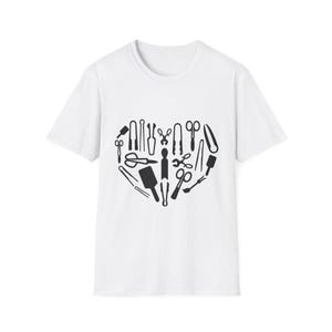 May include: White t-shirt featuring a heart-shaped design composed of various black tools. The tools include scissors, wrenches, and other implements, creating a unique and artistic graphic. The shirt is a classic crew neck style.