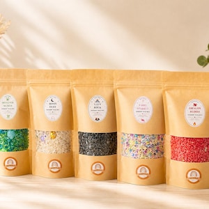 May include: Five stand-up kraft paper pouches containing sensory rice mixes. Each bag features a clear window displaying coloured rice: green, white, black, multicoloured, and red. Labels read Monster Munch, Moon Dust, Lava Rock, Fairy Sparkle, and Dragon Blood.