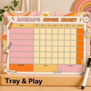 May include: A pink and orange chore chart with the text "AMELIA'S CHORE CHART". The chart includes sections for tasks and days of the week. A black and white marker is on a wooden base. The text "Tray & Play" is at the bottom. The design has a retro aesthetic.