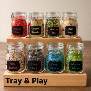 May include: Eight clear glass jars with wire-bail lids, filled with colourful sensory rice, arranged on a two-tiered wooden stand labelled Tray & Play. Labels read Dragon Blood, Unicorn Crunch, Meadow Mix, Moon Dust, Fairy Sparkle, Lava Rock, Ocean Breeze, and Monster Munch.