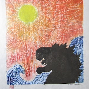 May include: A woodblock print of Godzilla standing in the ocean with a yellow sun in the sky. The print is in shades of red, orange, yellow, blue, and black. The print is signed "Kazu Otake" in the bottom right corner and numbered "7/5" in the bottom left corner.