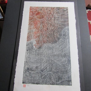 May include: A black and white woodcut print depicting a sun and waves. The sun is red and orange with a radiating pattern. The waves are black and white and are stylised.