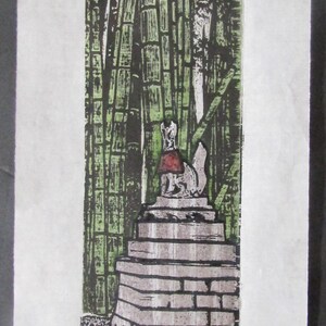 Puede incluir: Una impresión en madera en blanco y negro de una estatua de zorro de piedra en un bosque de bambú. El zorro lleva un babero rojo y está sentado en una plataforma de piedra con escalones. La impresión está firmada "Kevin Clark" en la esquina inferior derecha y tiene un sello rojo en la esquina inferior izquierda.