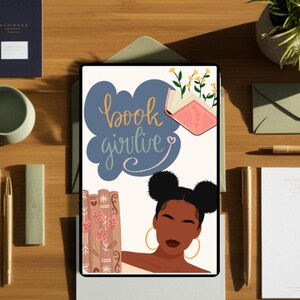 May include: Digital art print featuring a Black woman with two buns and gold hoop earrings. The artwork includes the text "book girlie" in a cloud-shaped design, a stack of books, and an open book with flowers. The print is on a tablet.