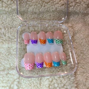 May include: A set of artificial nails in a clear plastic case. The nails are a natural pink color with colorful polka dot designs on the tips. The polka dots are pink, purple, orange, turquoise, and green.