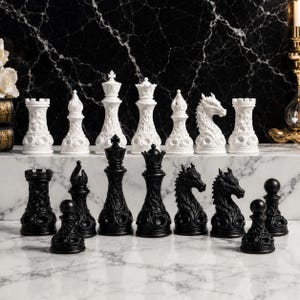 Può includere: Un set di scacchi completo con pezzi neri e bianchi. I pezzi bianchi includono torri, alfieri, una regina e un re. I pezzi neri includono torri, alfieri, una regina e un re. I pezzi degli scacchi sono disposti su una superficie di marmo.
