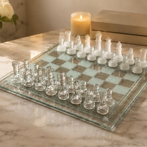 Op de afbeelding: Een glazen schaakspel met een vierkant bord met afwisselend heldere en matglazen vakjes. De set bevat een complete collectie van transparante heldere glazen schaakstukken en doorschijnende matglazen schaakstukken in de beginopstelling.