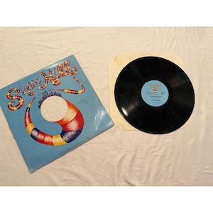 May include: A vintage vinyl record album with a light blue cover featuring the words "Sugar Hill" in a colorful, stylized font. The album art includes a large, abstract design with rainbow colors. The black vinyl record is visible next to the album cover.