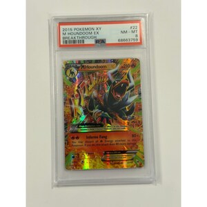 May include: A Pokemon trading card featuring Mega Houndoom. The card has a holographic design with a fiery background and the text "Inferno Fang." The card is graded and encased in a protective holder with the text "2015 Pokemon XY M Houndoom EX Breakthrough."